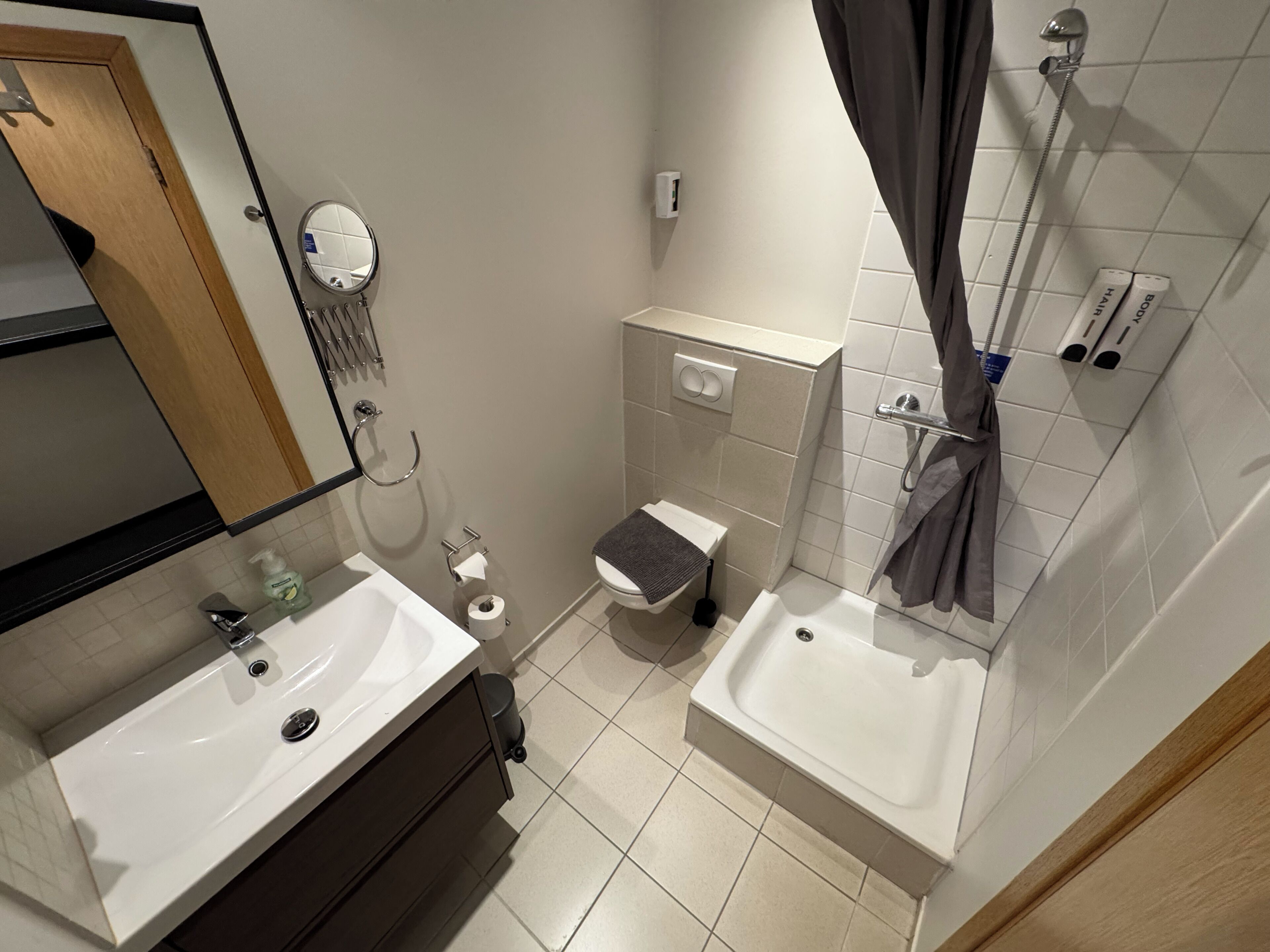 Ein Badezimmer mit zwei Waschbecken, einer Toilette, einem Spiegel, einem Handtuchhalter und einer Dusche.