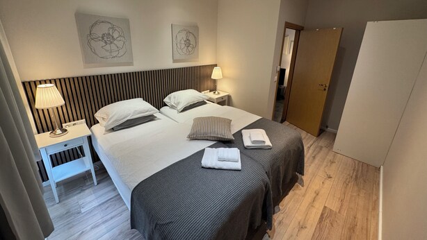 A hotel room with two beds, a wooden floor, a white wardrobe, and artwork on the walls.