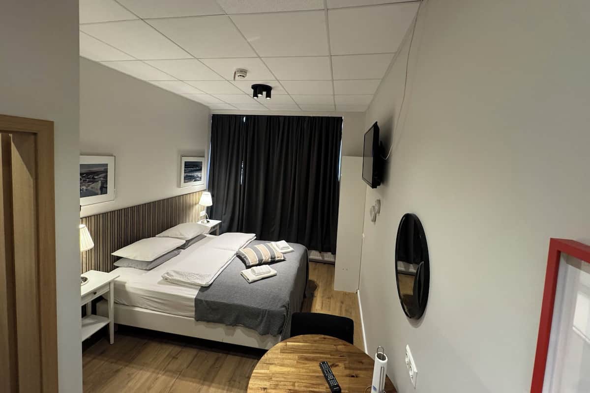 A hotel room with a bed, bedside table, lamp, TV, and a small round table.