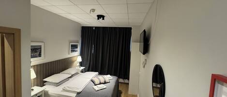 A hotel room with a bed, bedside table, lamp, TV, and a small round table.