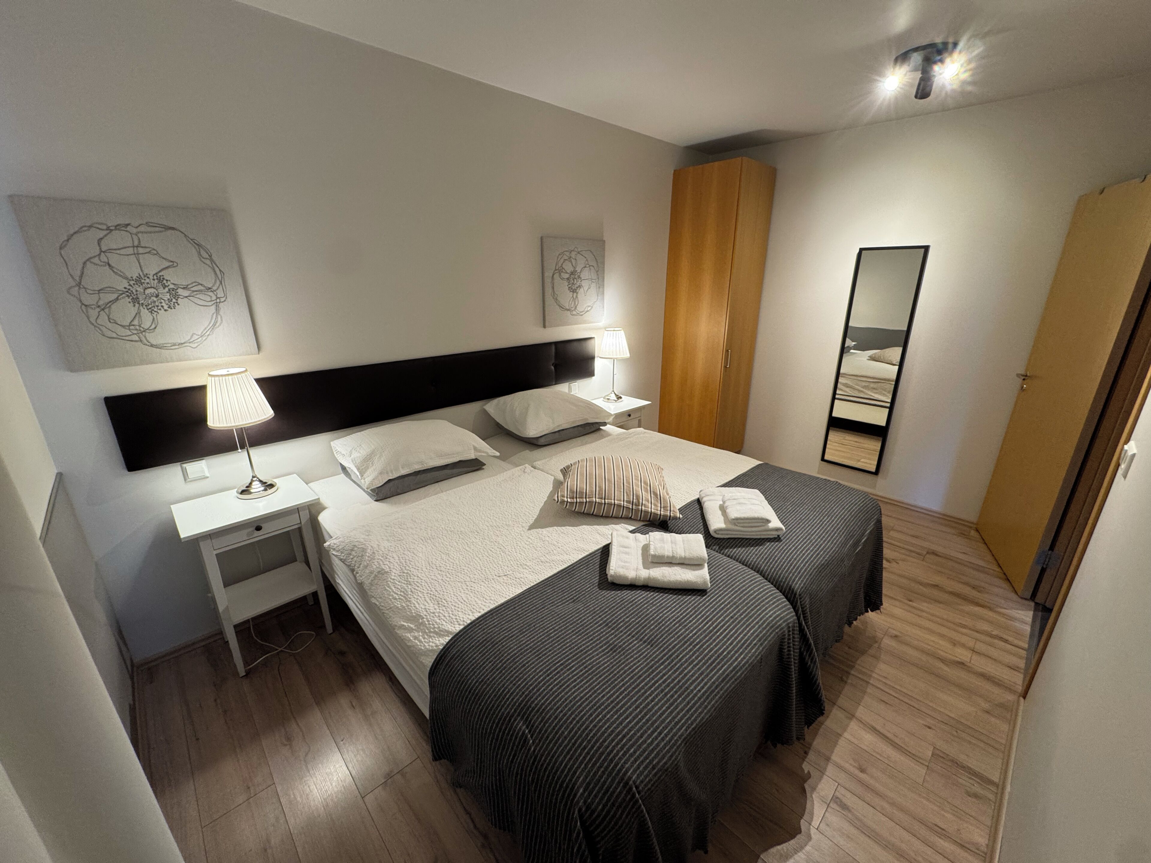 A hotel room with two beds, a nightstand, a lamp, a wardrobe, and a mirror.