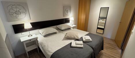 A hotel room with two beds, a nightstand, a lamp, a wardrobe, and a mirror.