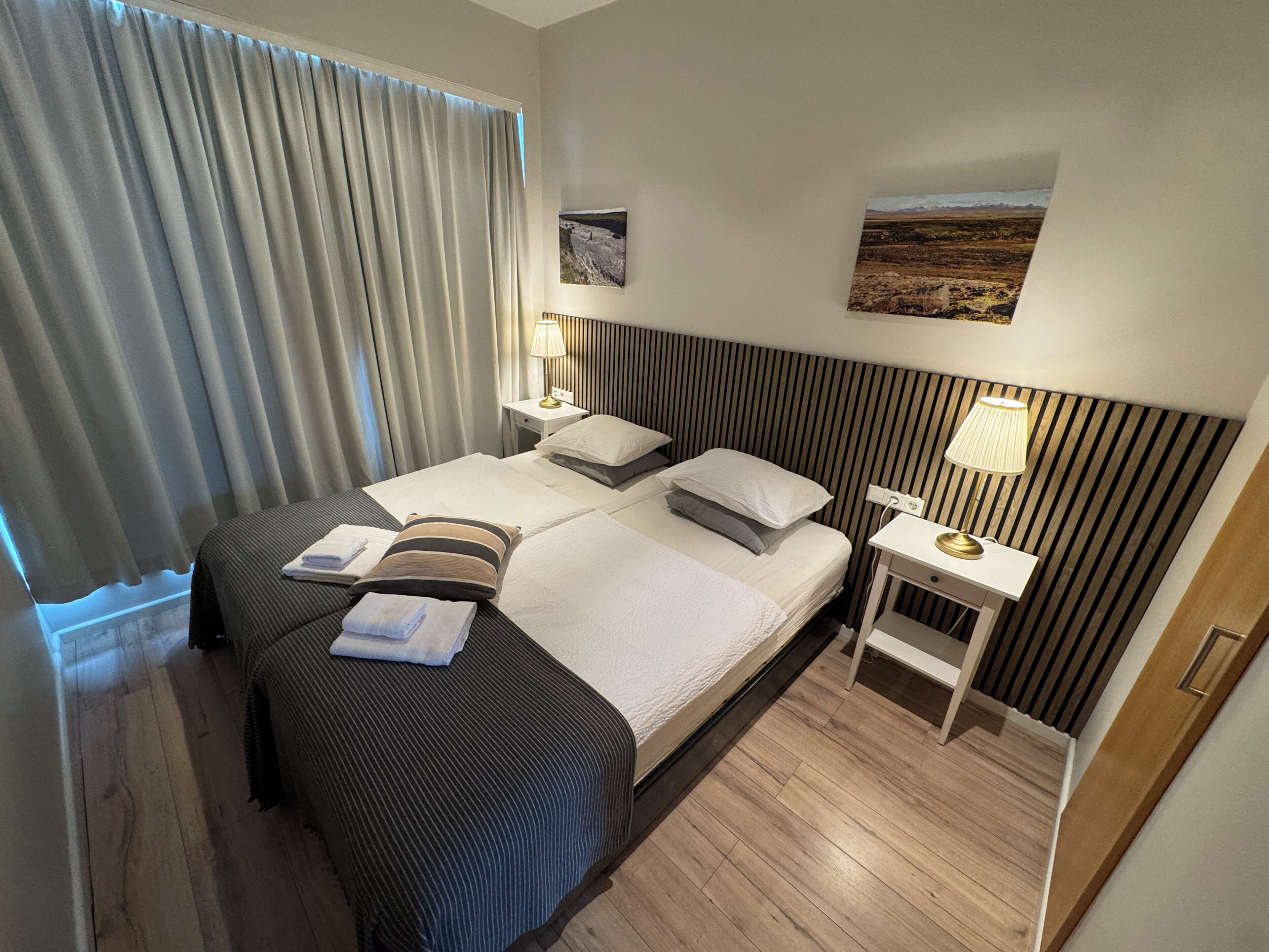 Une chambre d’hôtel avec un lit, deux tables de chevet, une petite table, une lampe et un tableau au mur.