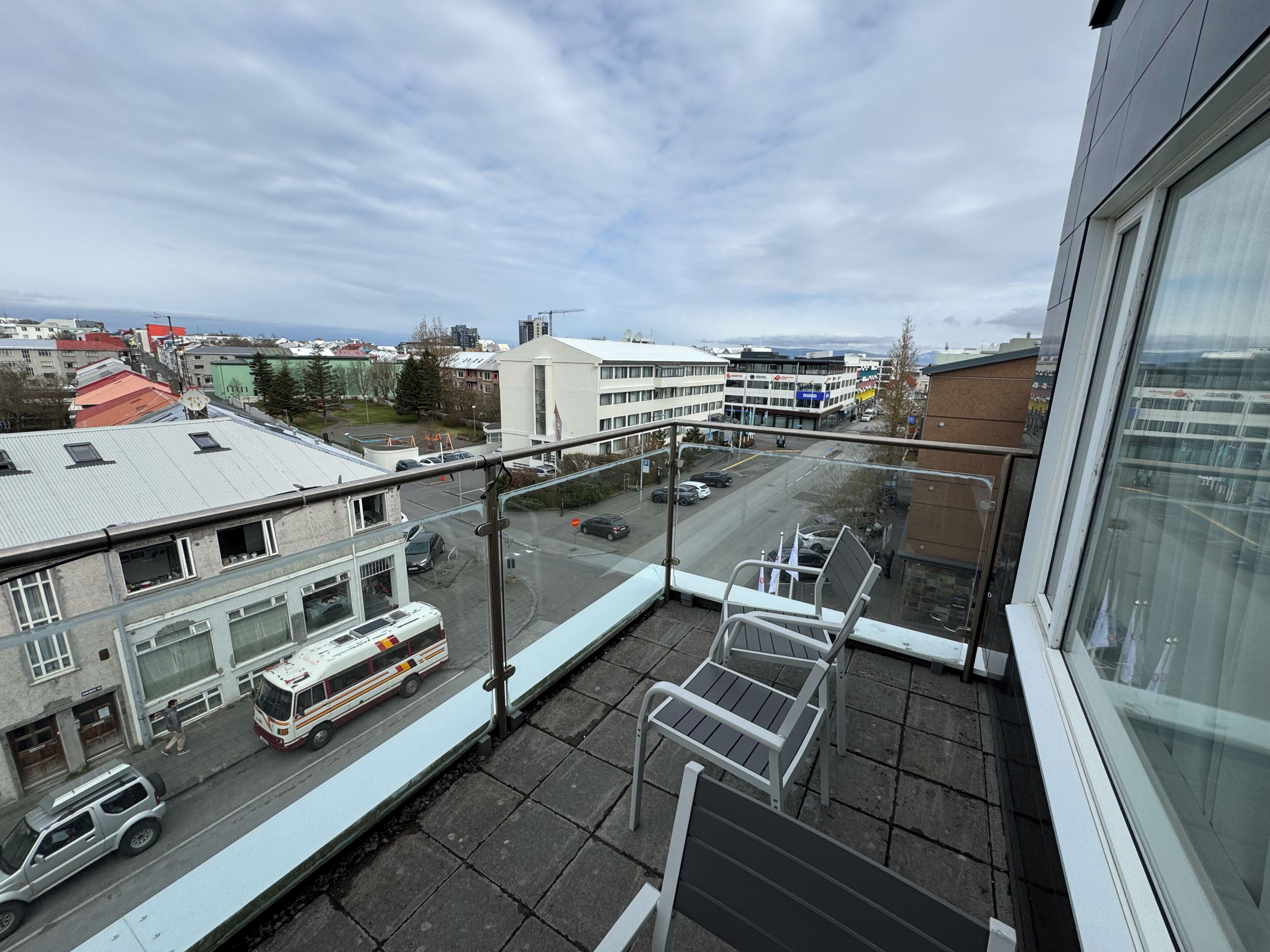 Een balkon met uitzicht op een stadsstraat, een bus en gebouwen.