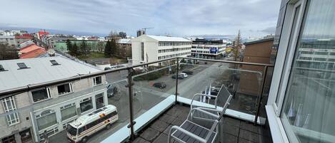 Een balkon met uitzicht op een stadsstraat, een bus en gebouwen.