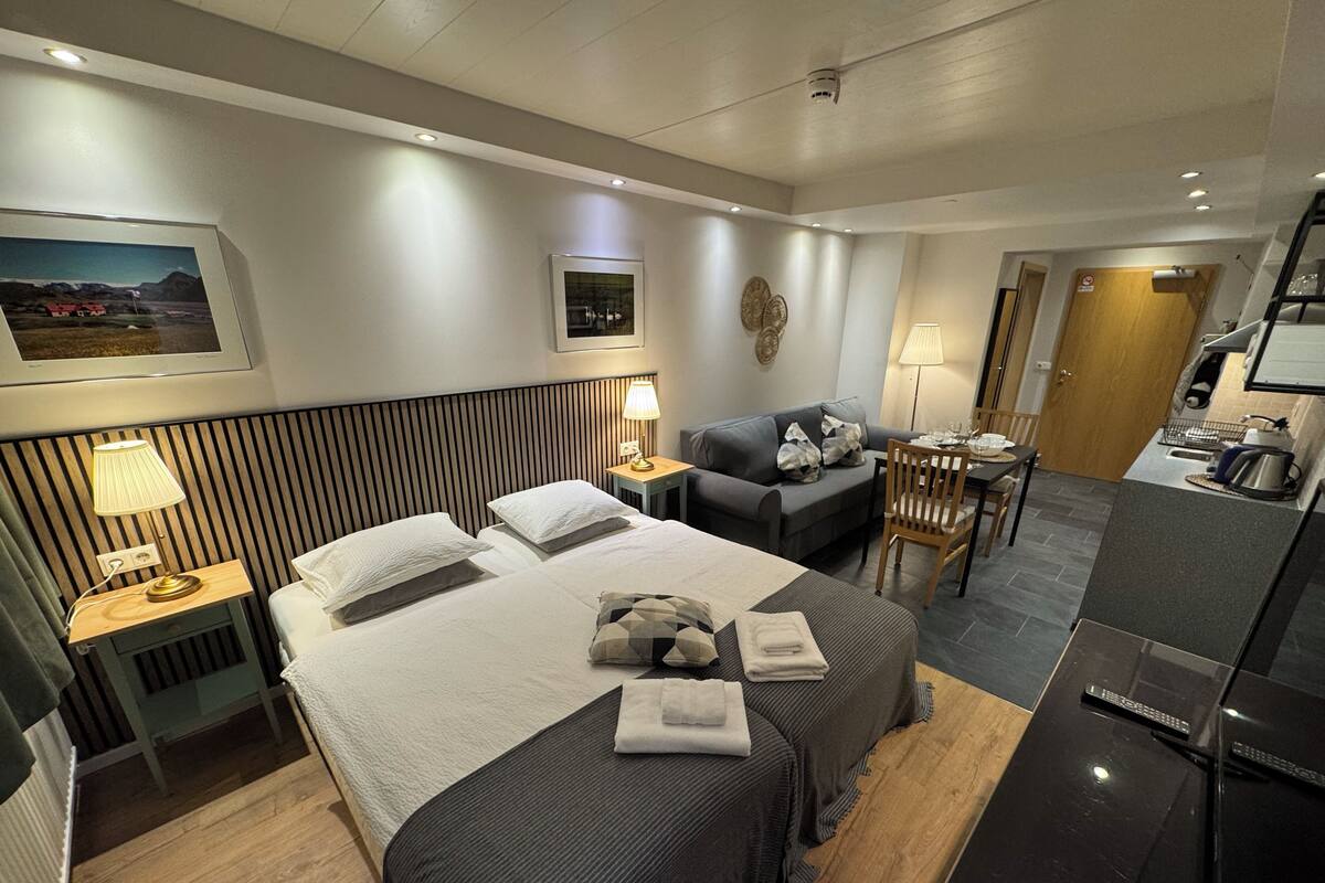 A hotel room with two beds, a sofa, a dining table, and a kitchenette.