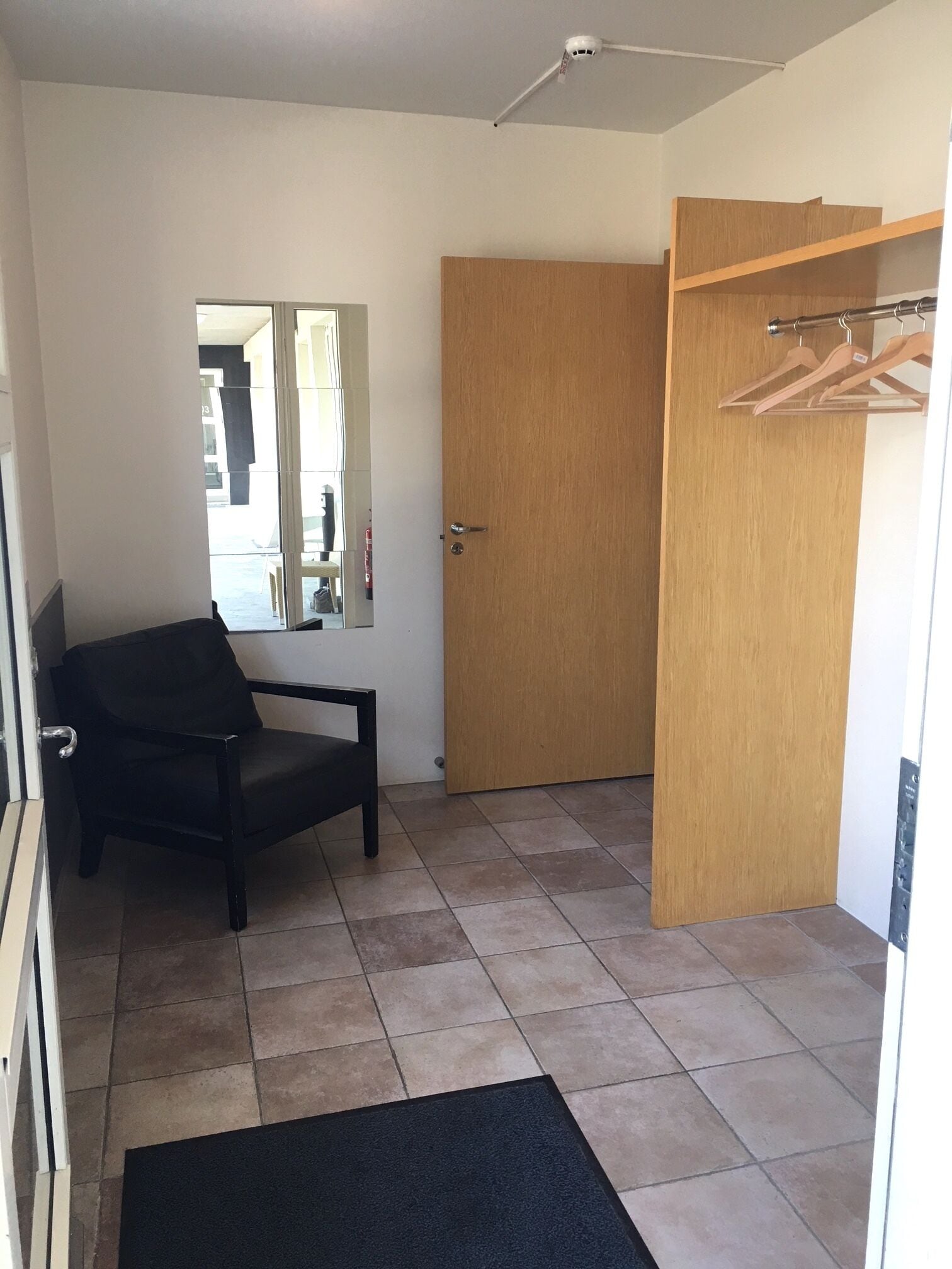 A room with a black chair, a wooden door, and a wooden wardrobe with hangers.