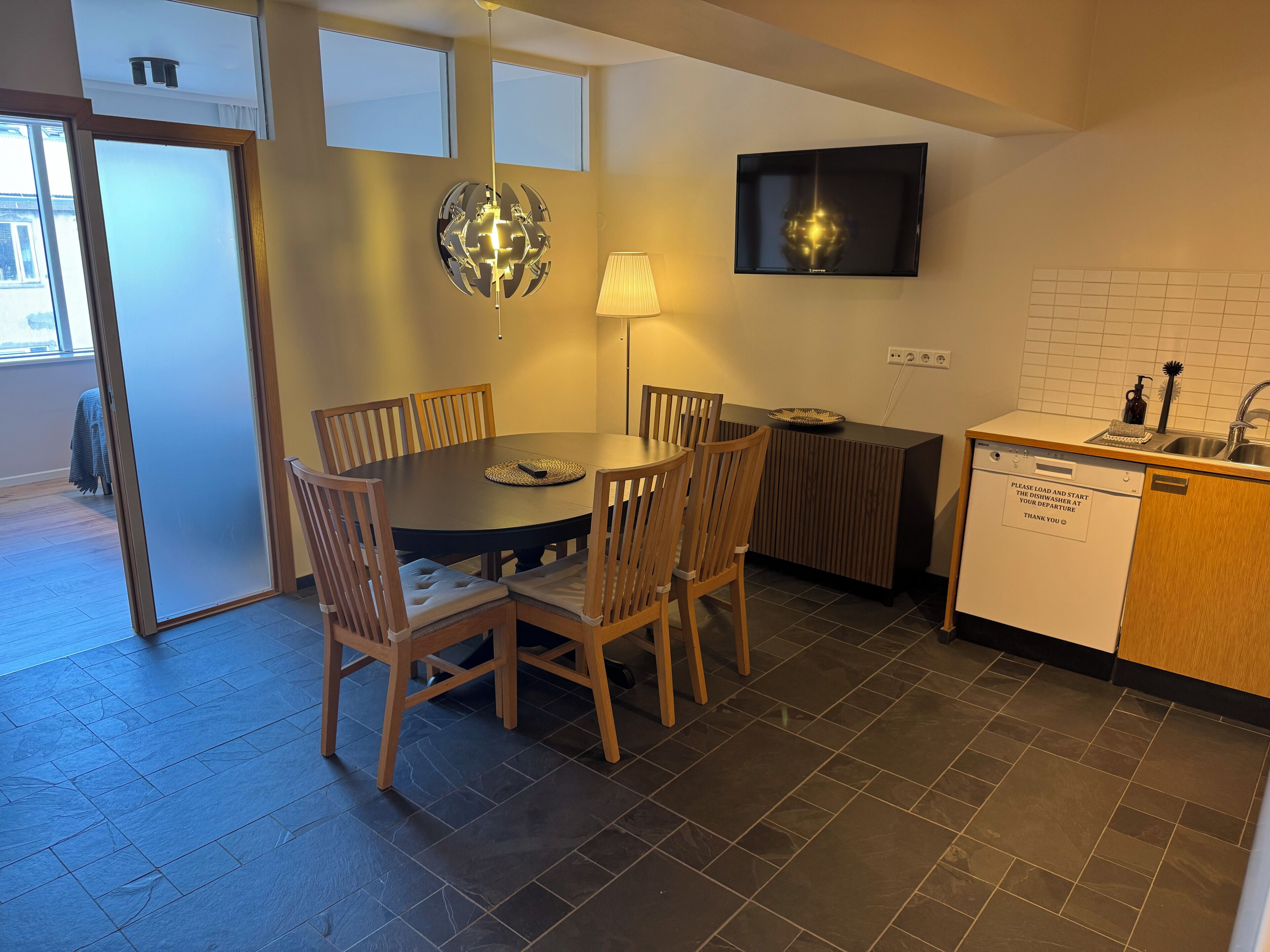 Een compacte keuken met een eethoek, een aan de muur bevestigde televisie en een inbouw vaatwasser.