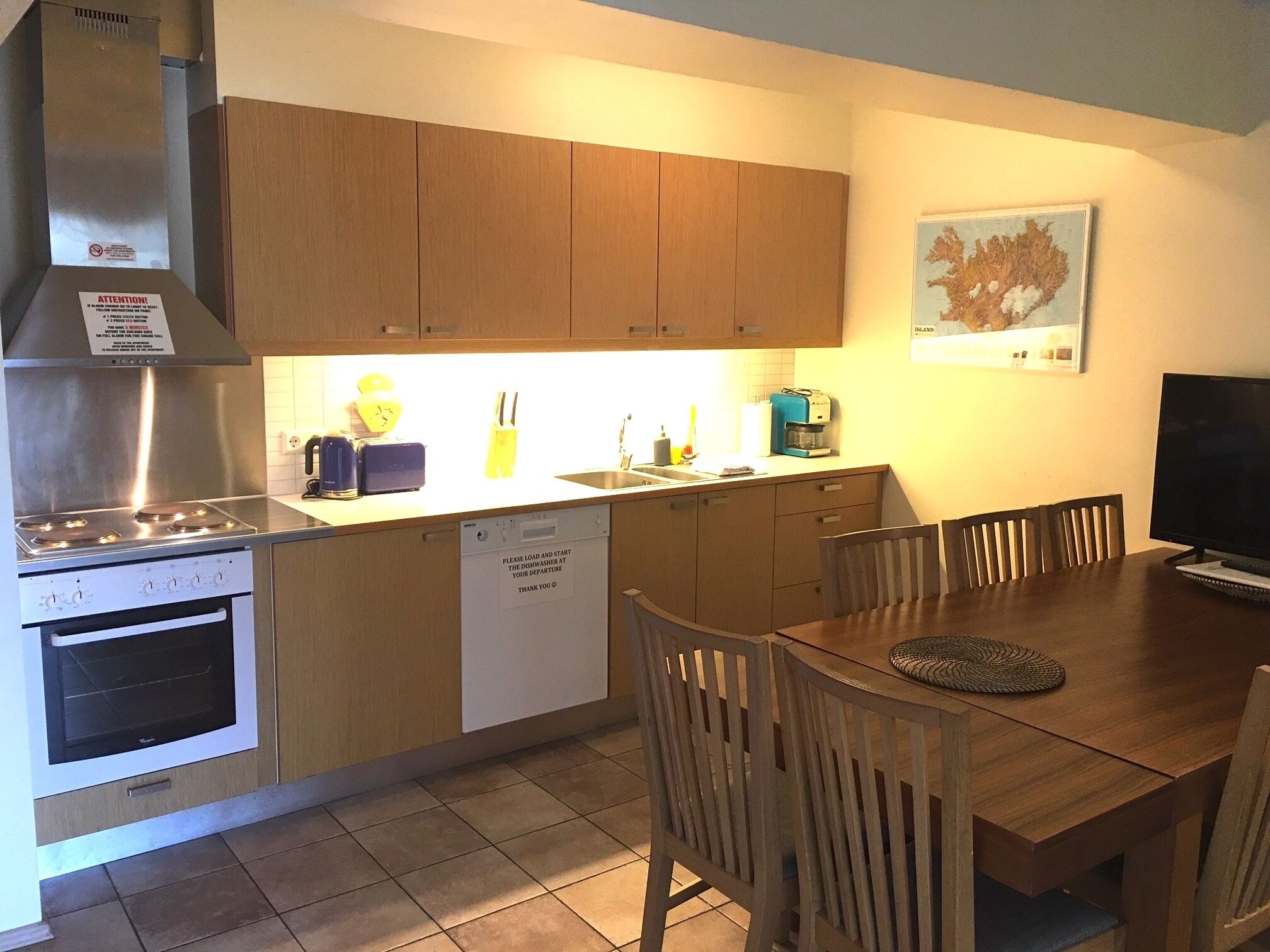 Una cocina compacta con armarios de madera, estufa de acero inoxidable, lavavajillas y un comedor con mesa y sillas.