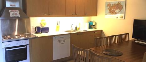 Una cocina compacta con armarios de madera, estufa de acero inoxidable, lavavajillas y un comedor con mesa y sillas.