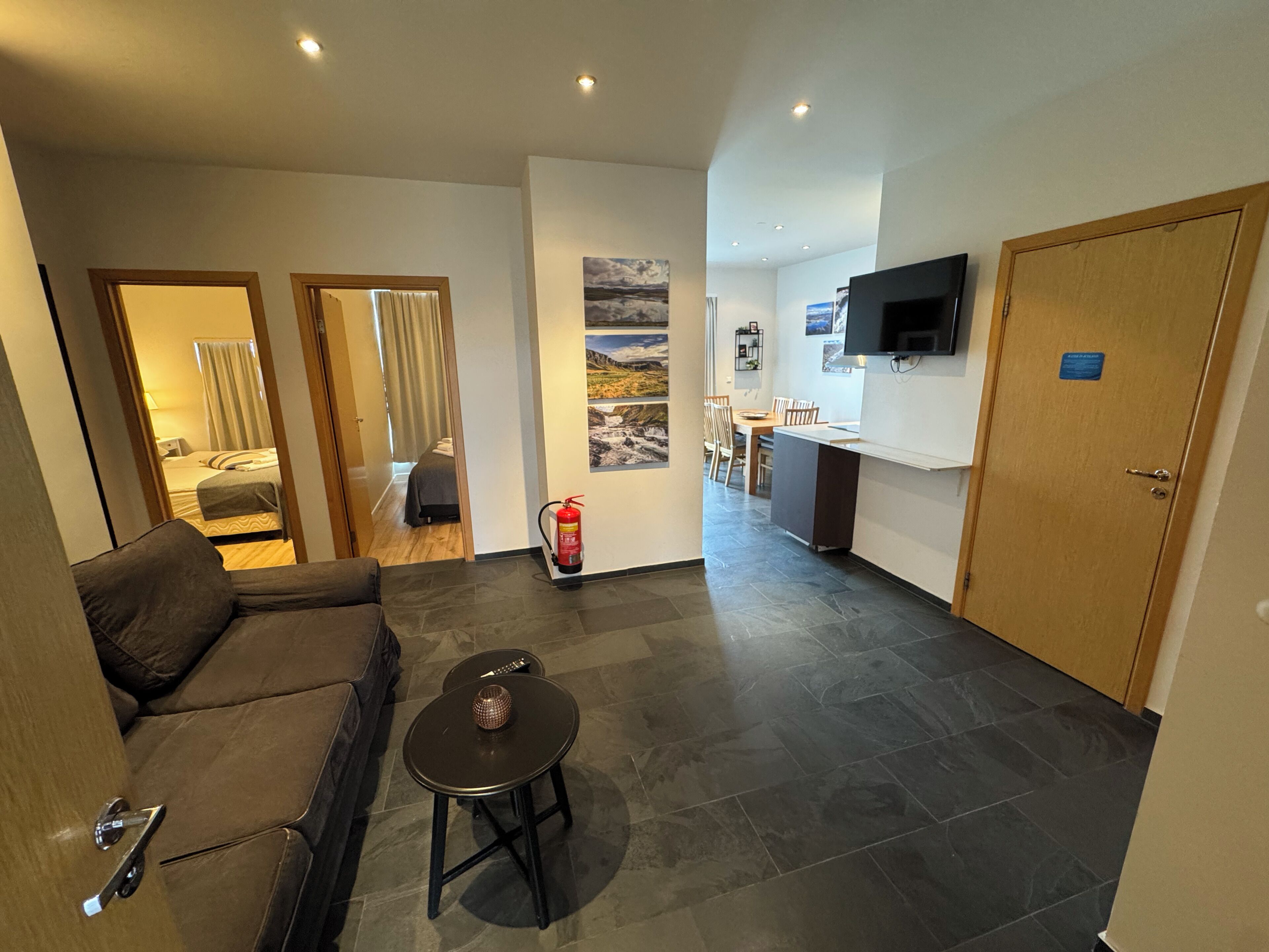 Una habitación de hotel moderna con sofá, una pequeña mesa, cama, baño, zona de cocina y televisor.