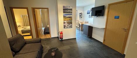 Una habitación de hotel moderna con sofá, una pequeña mesa, cama, baño, zona de cocina y televisor.
