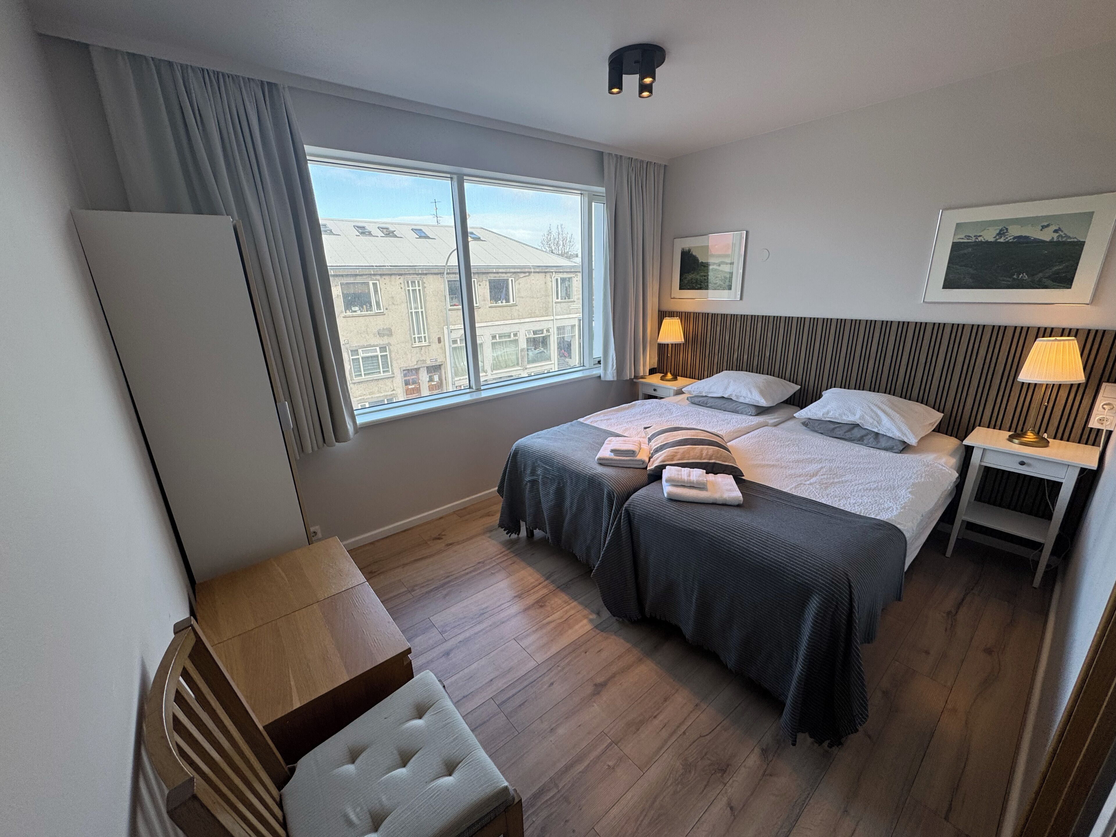 A hotel room with a large window, two beds, a desk, and a chair.