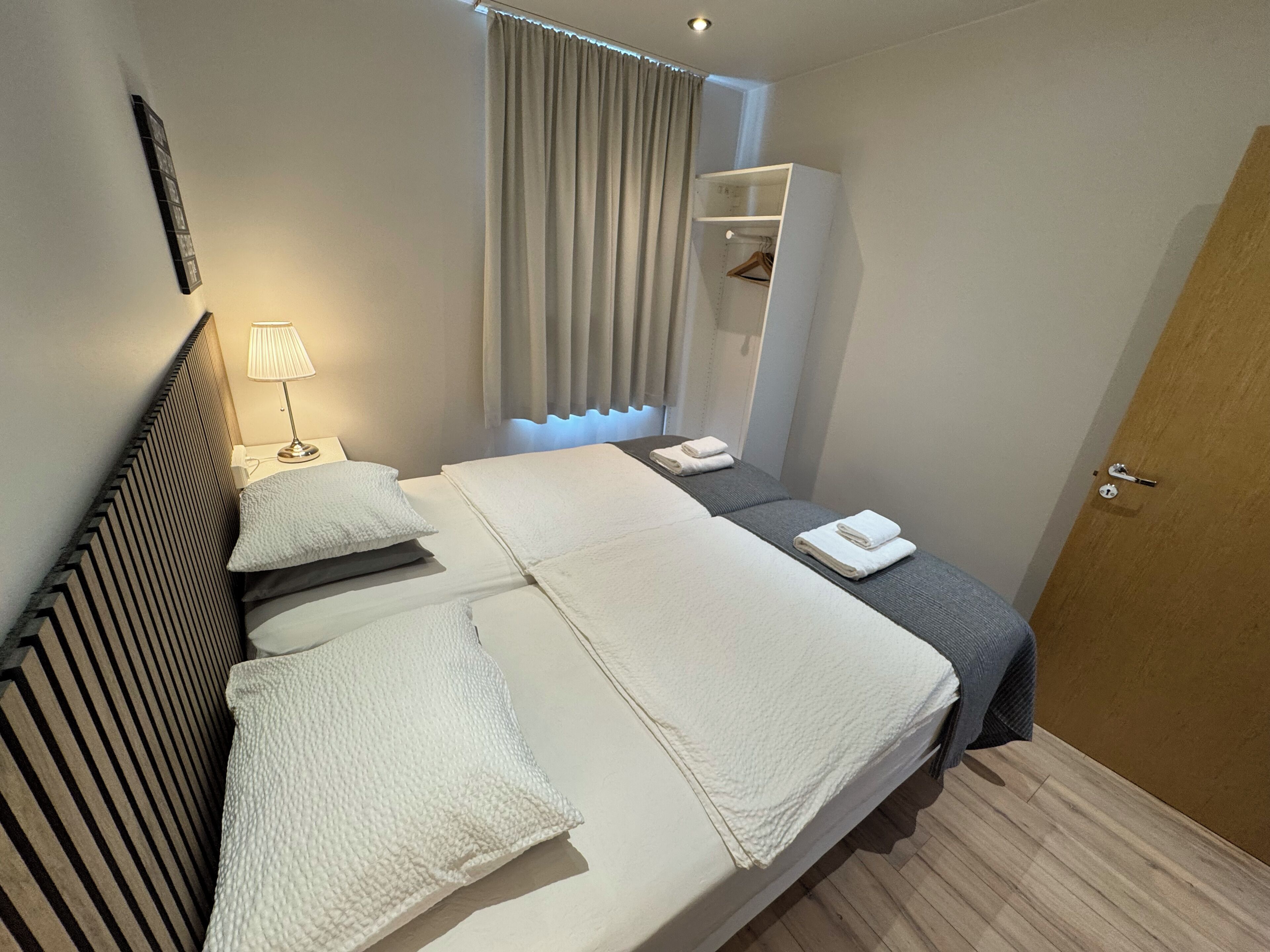 Ein Hotelzimmer mit Bett, Nachttischen, einer Lampe, einem Kleiderschrank und einer Tür.
