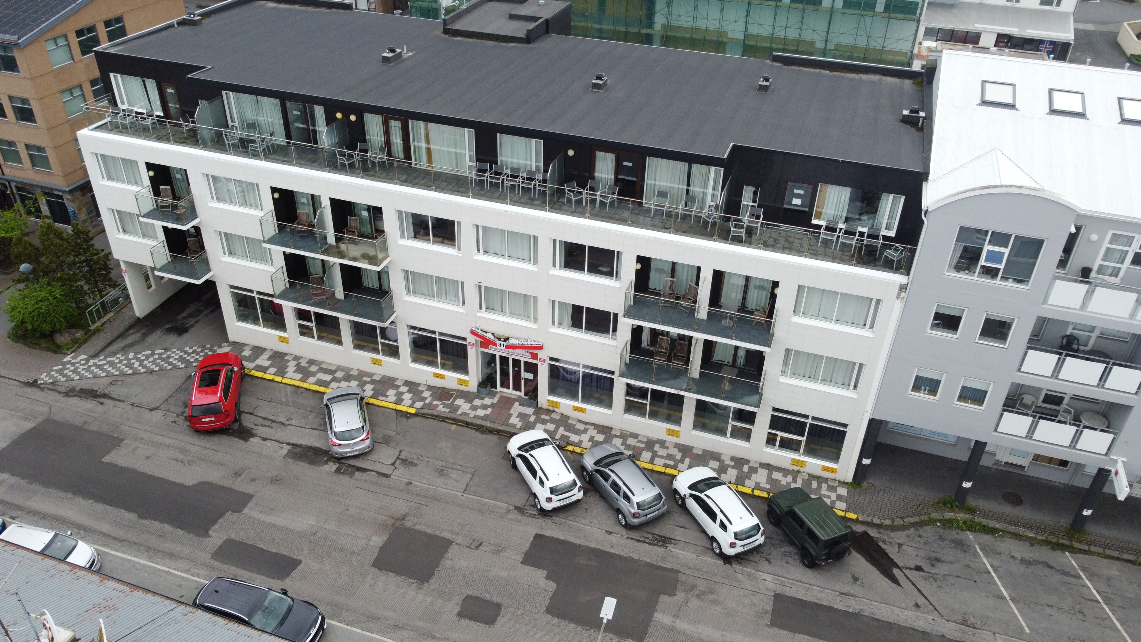 A multi-story hotel with balconies, a checkered pavement, and parked cars.
