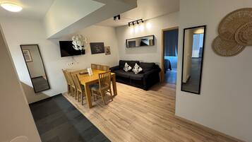 A modern living room with a dining area, a black sofa, and a TV mounted on the wall.