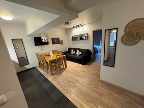 A modern living room with a dining area, a black sofa, and a TV mounted on the wall. - Downtown Reykjavík Apartments (Reykjavik)