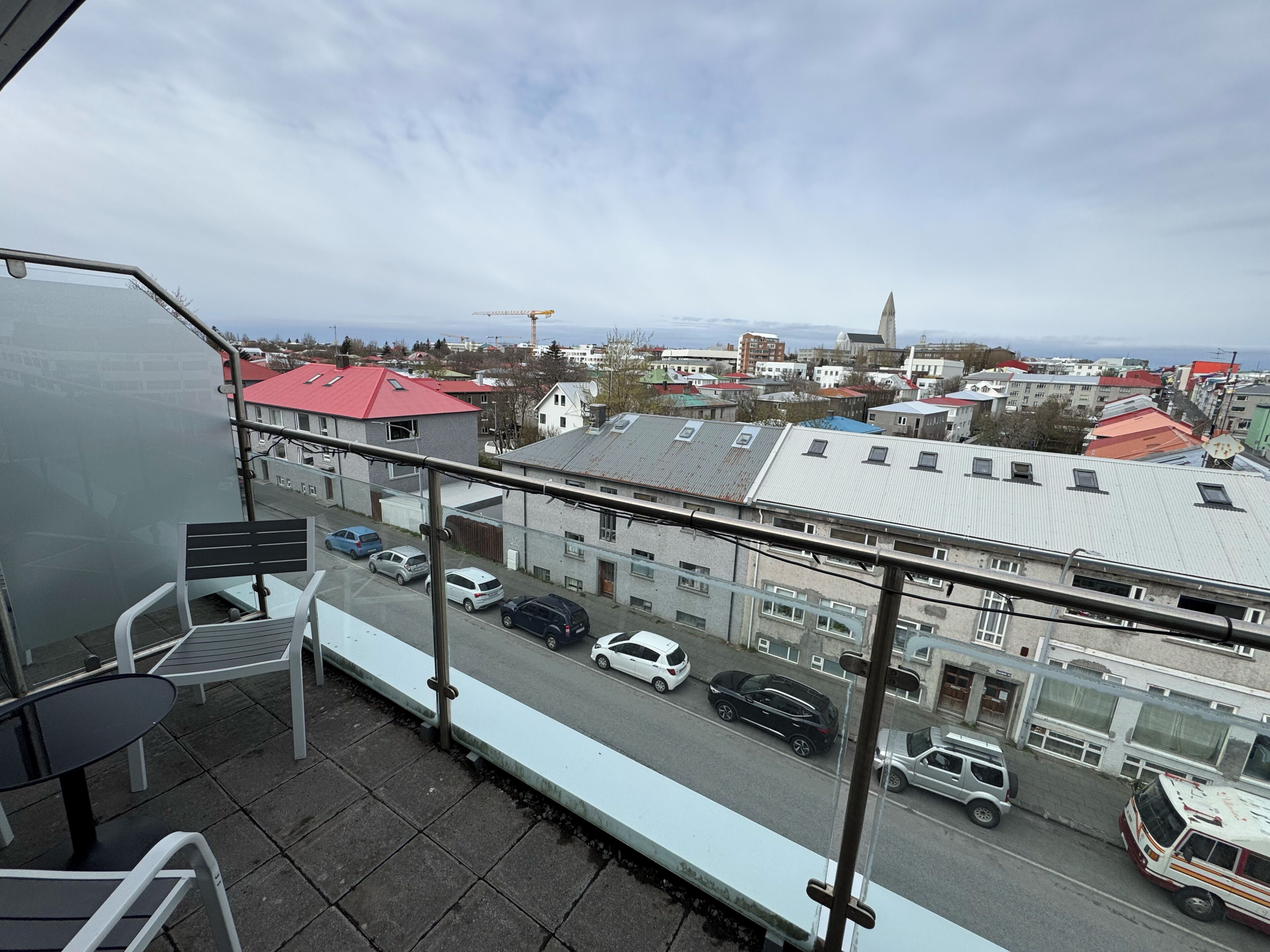 A balcony with a view of a cityscape, including buildings and parked cars.