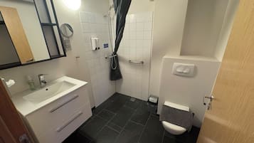 A bathroom with a white sink, a mirror, a shower with a curtain, and a toilet.