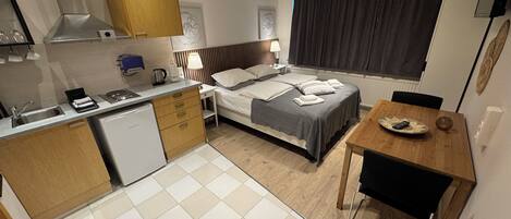 Une chambre d’hôtel compacte comprenant un coin cuisine, un lit avec une tête de lit, une table à manger et une grande fenêtre.
