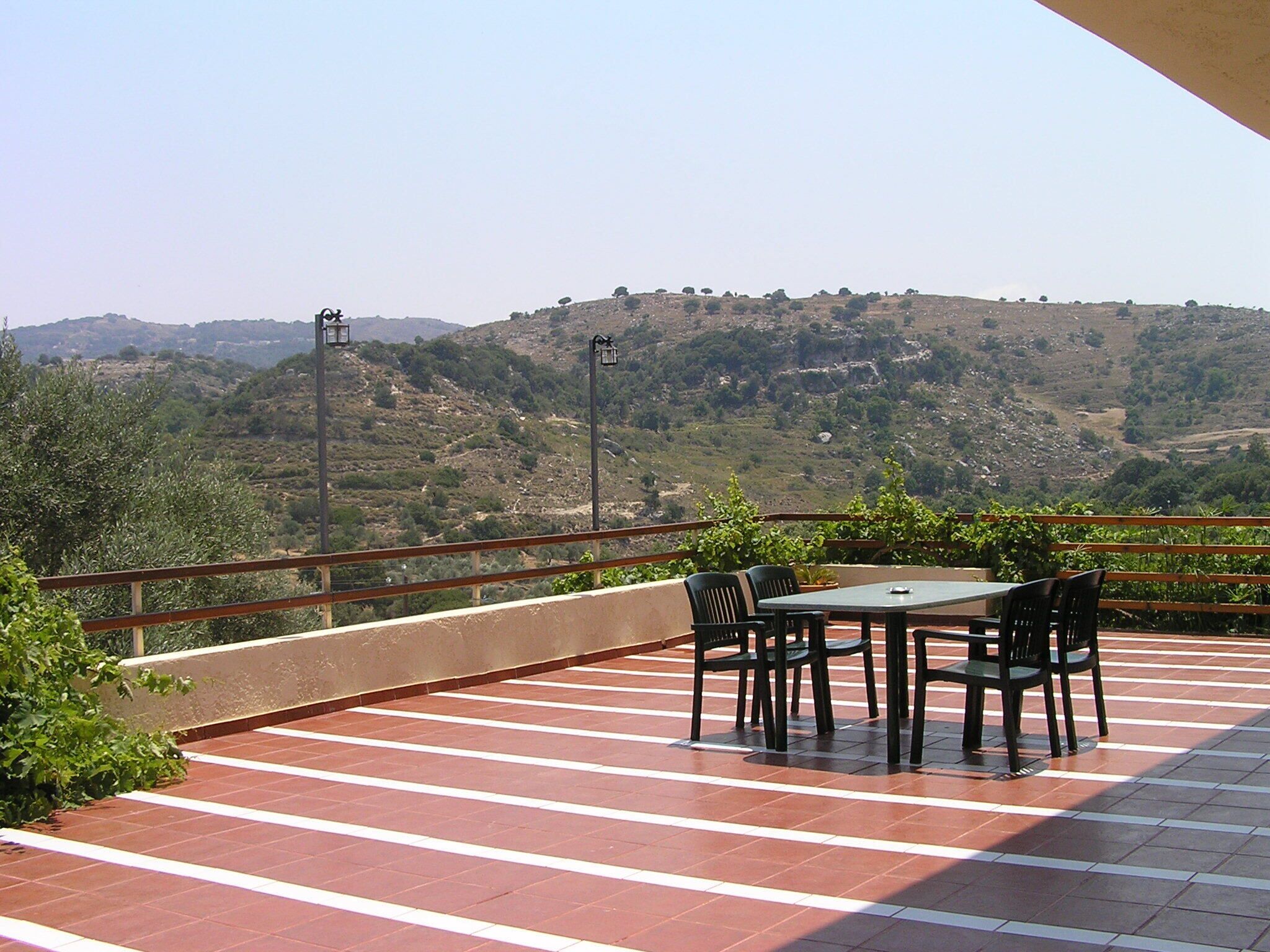 Eine Terrasse mit Tisch und Stühlen mit Blick auf eine hügelige Landschaft.