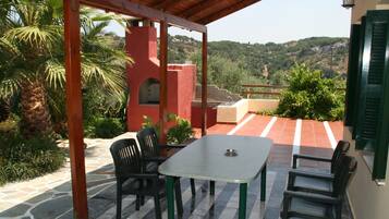 A covered patio with a table and chairs, a stone floor, and a view of a hillside.