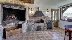 A stone-built outdoor kitchen with a fireplace, stone shelves, and a view of the countryside.