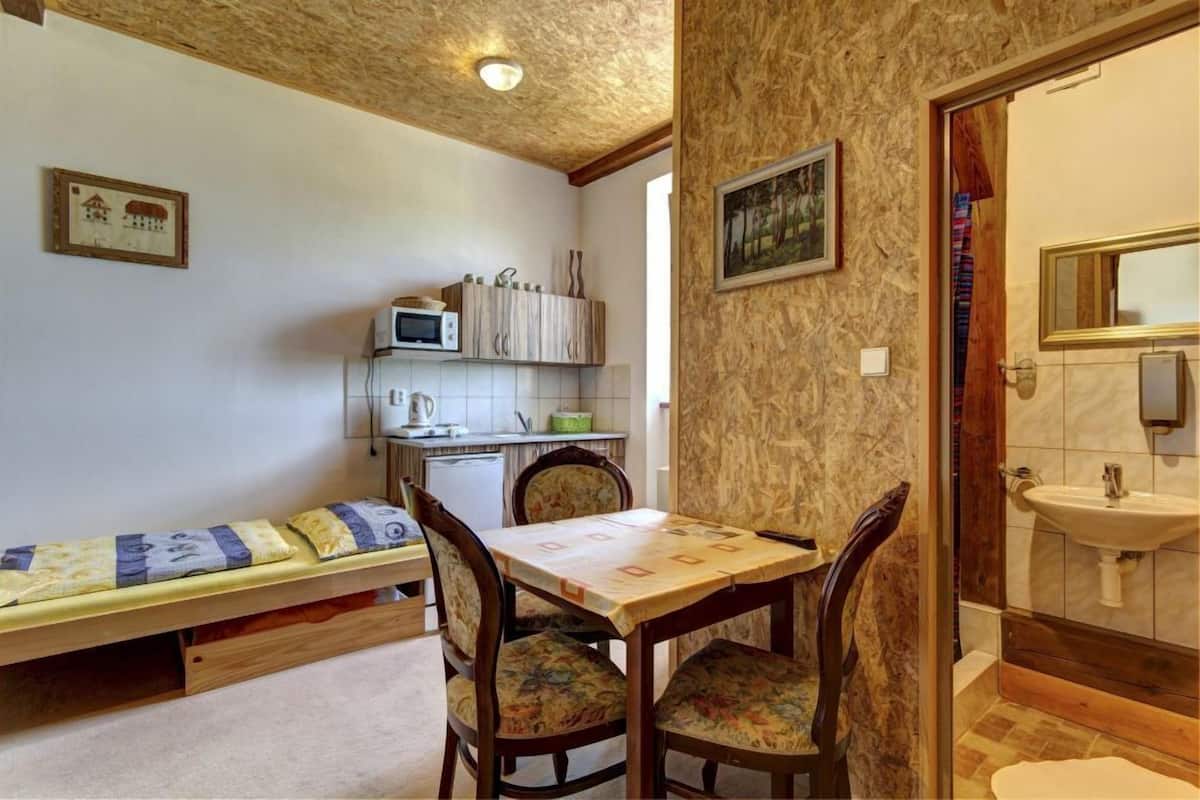 Una habitación compacta con cama, una pequeña mesa con sillas, kitchenette y baño.