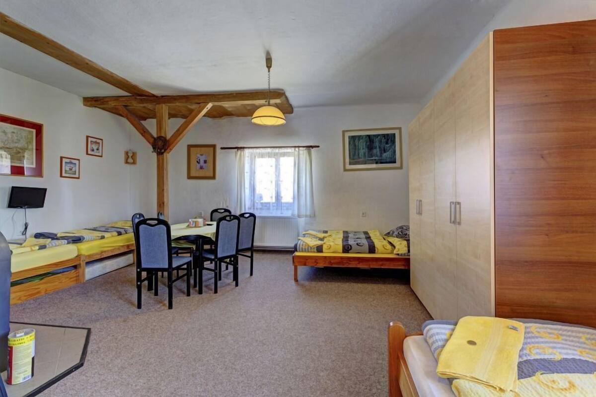 Una habitación con techo de madera, una mesa de comedor con sillas, una cama con una colcha amarilla y un armario de madera.