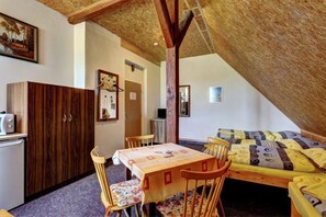 Une pièce mansardée chaleureuse avec un plafond en bois, une table à manger avec des chaises, un lit avec une literie à motifs et une armoire.
