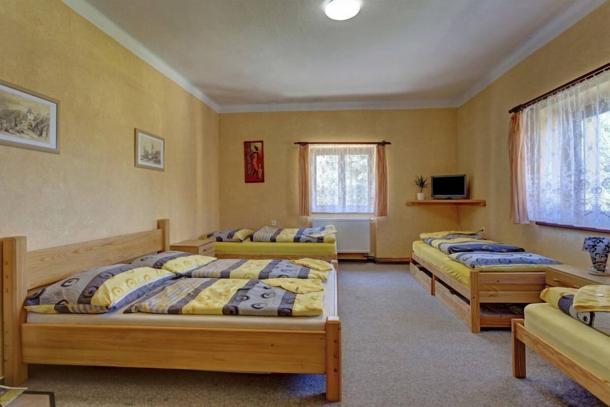 Una habitación con tres camas de madera, un televisor pequeño sobre una estantería y una ventana con cortinas.