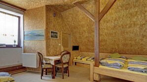 A room with a wooden ceiling, a dining table with chairs, a bed with pillows, and a painting on the wall.