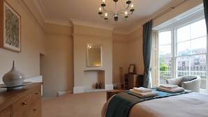 A hotel room with a large bed, a dresser, a mirror, and a window with a view of buildings.