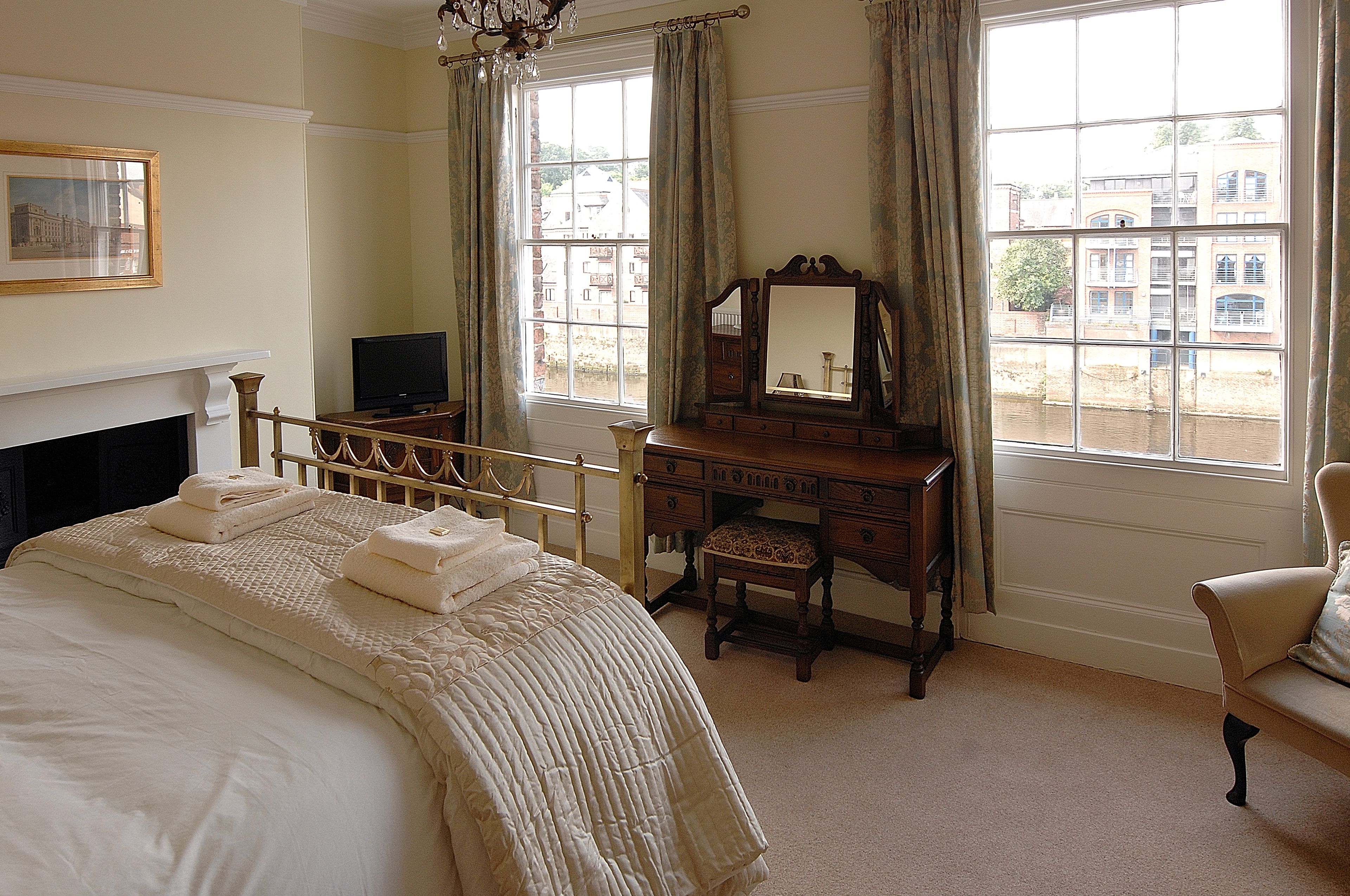 A bedroom with a bed, a dresser, a chair, a television, and a window with a view of buildings.