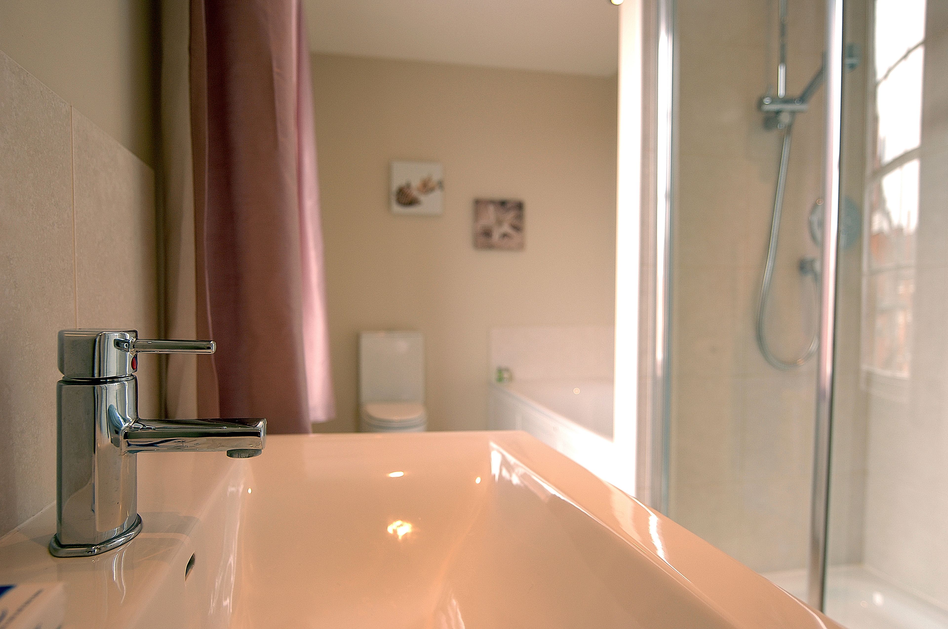 Un baño con grifo cromado, cabina de ducha con mampara de vidrio y un inodoro a simple vista al fondo.