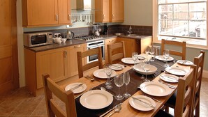 A kitchen with wooden cabinets, a dining table set for six with plates, glasses, and cutlery.