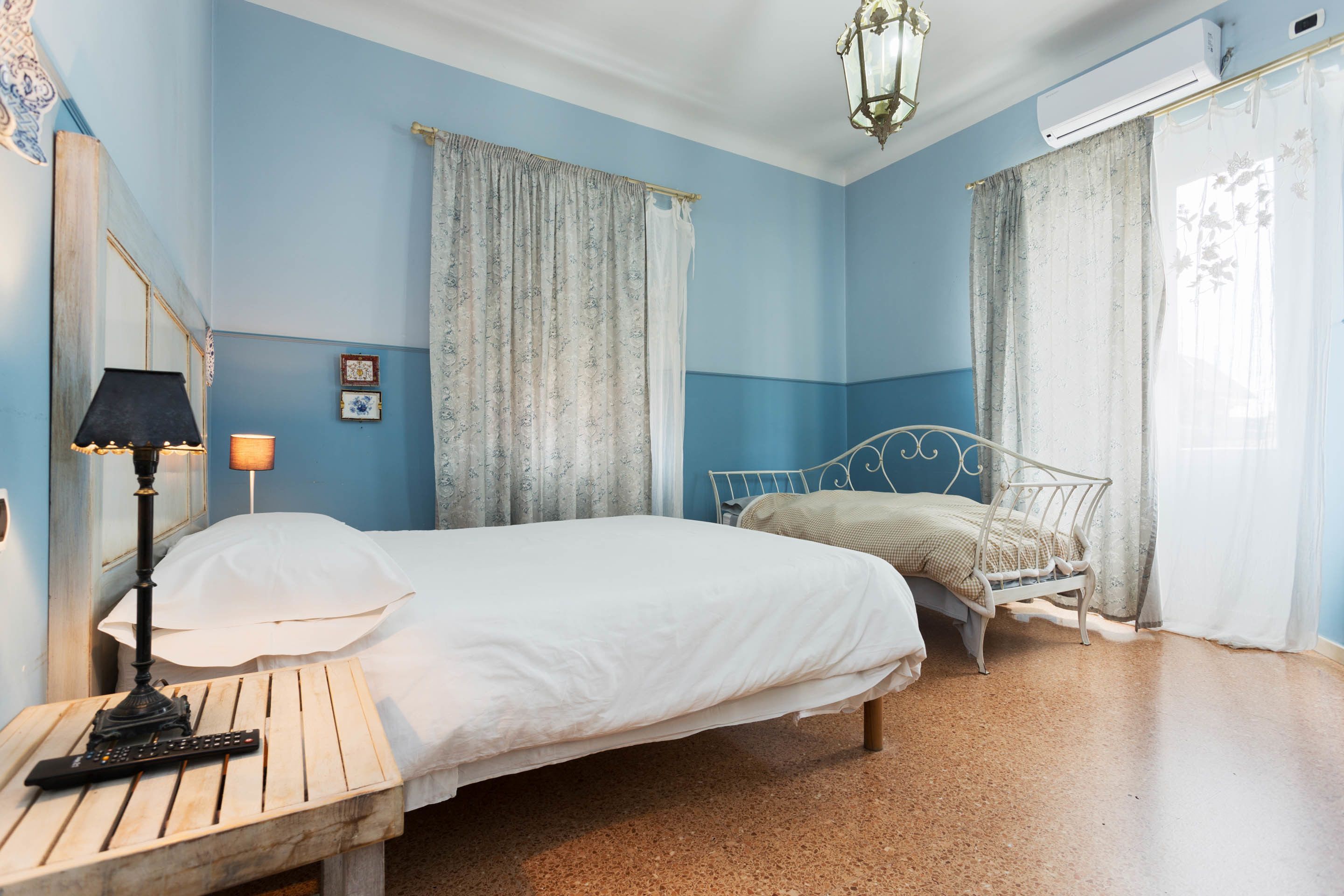 Una camera da letto con un letto, un comodino con una lampada, uno specchio e delle tende.