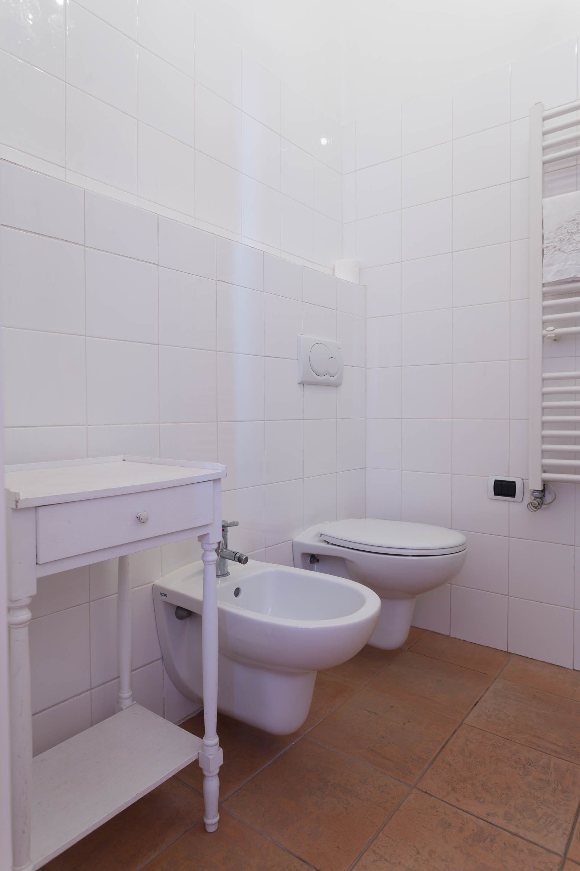 A bathroom with white tiles, a sink, a bidet, and a toilet.