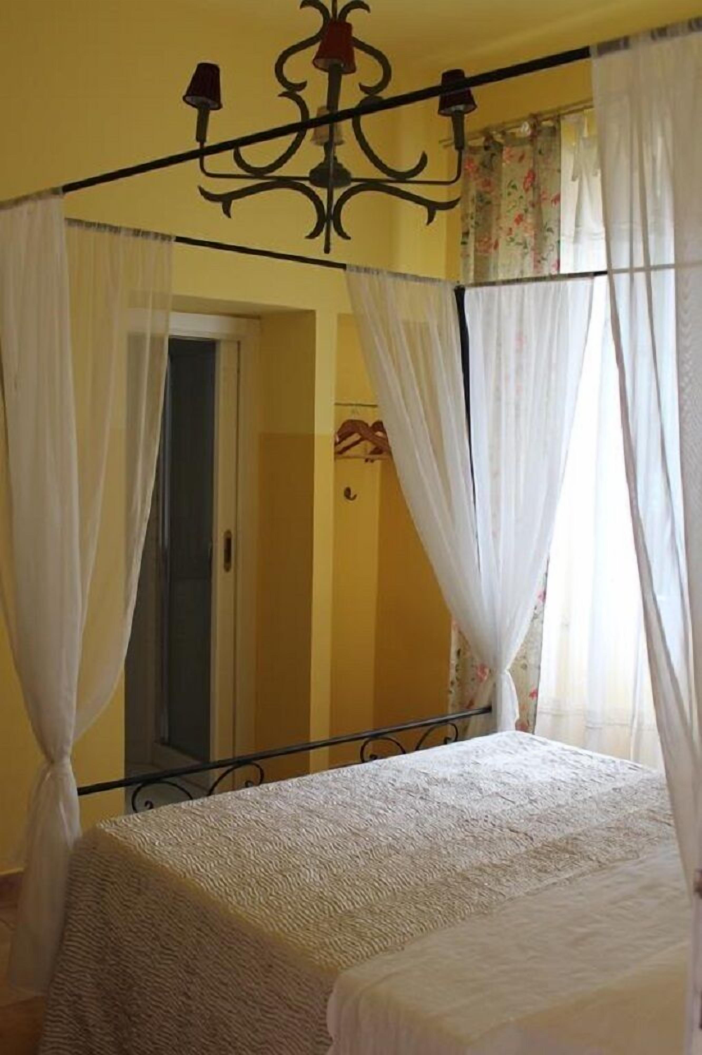 A four-poster bed with white curtains, a chandelier, and a view of a bathroom with a shower curtain.