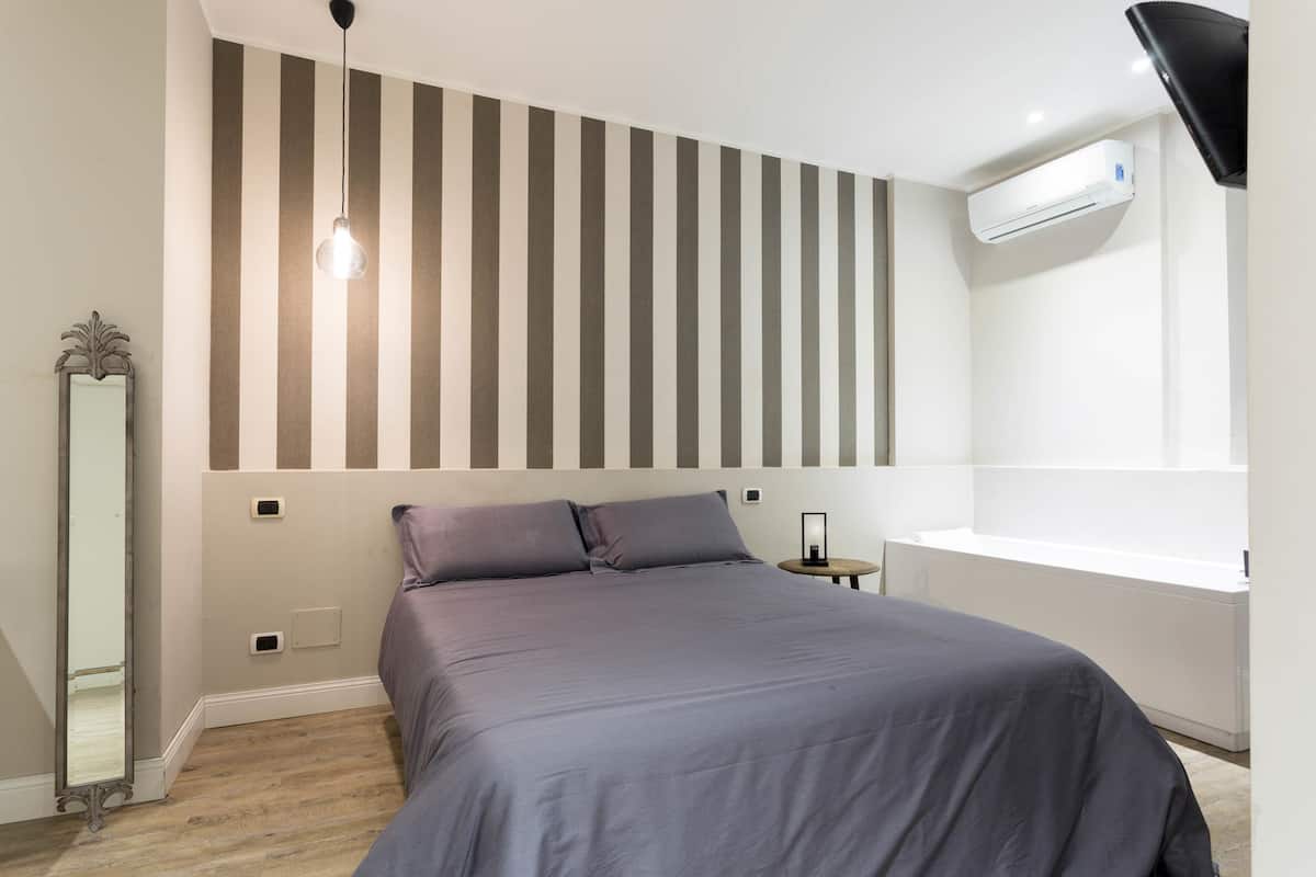 Un dormitorio con cama, mesita de noche, espejo y aire acondicionado instalado en la pared.
