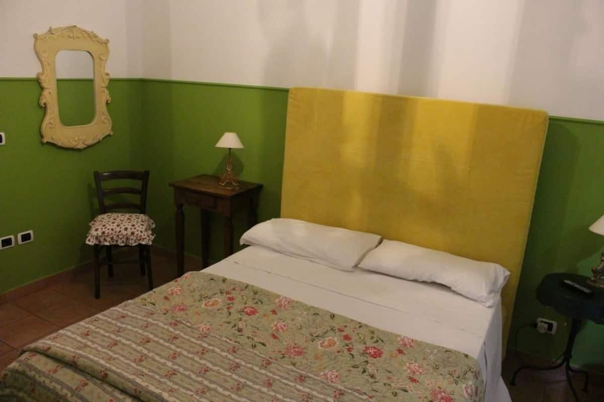 Una habitación con una cama, una silla, una mesita de noche con una lámpara y un espejo en la pared.