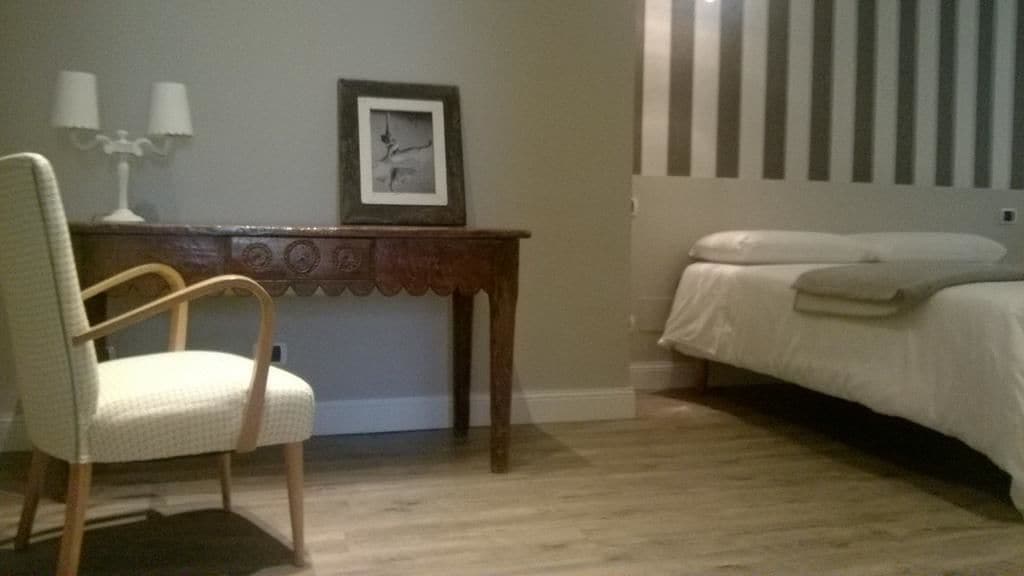 A hotel room with a wooden desk, a chair, a bed with white bedding, and a striped wall.