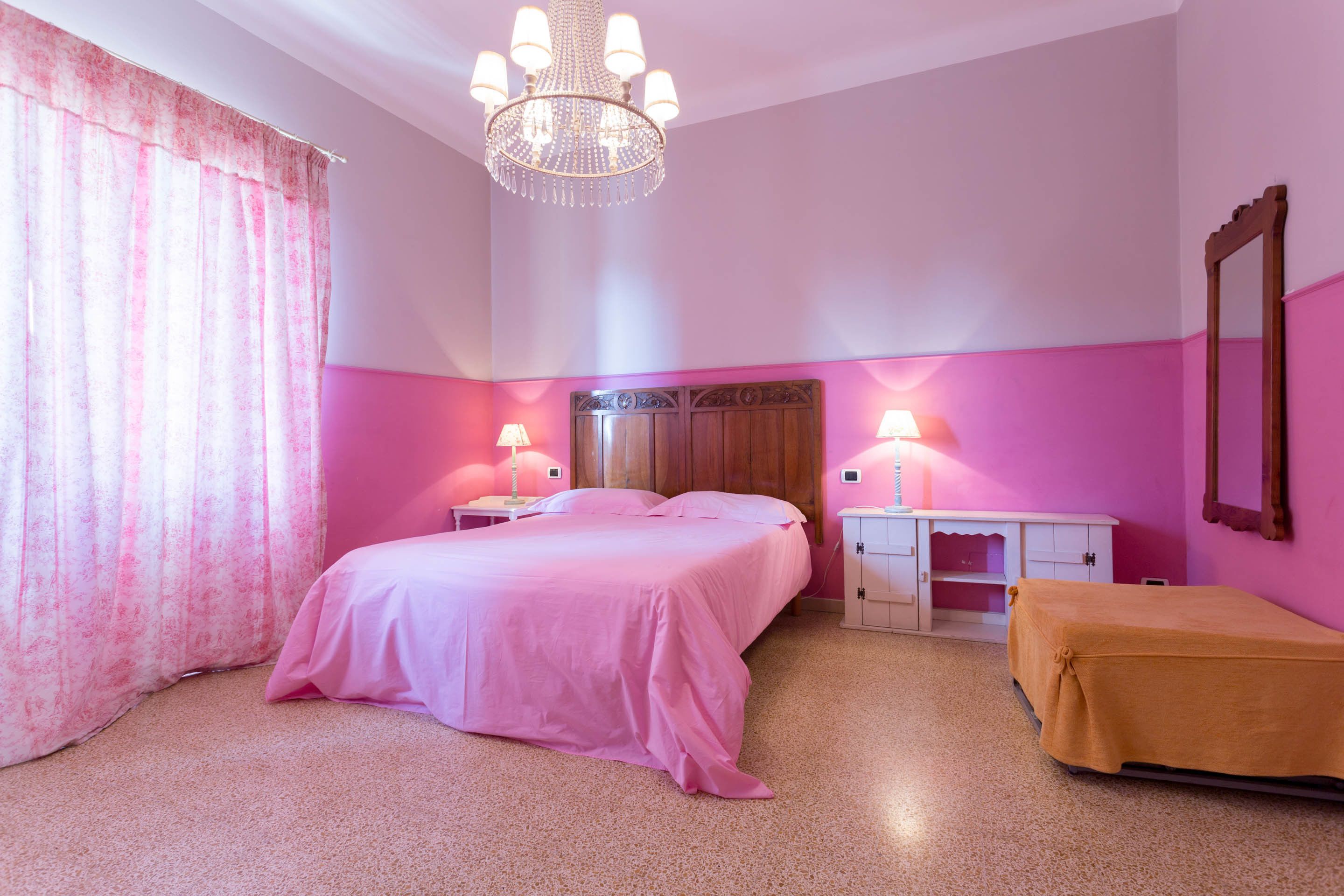A bedroom with a bed, bedside tables, a nightstand, a dresser, a mirror, and a chandelier.