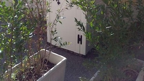 Un cobertizo pequeño y blanco con techo a dos aguas, una ventana y dos letreros negros con la letra 'H' en la puerta.