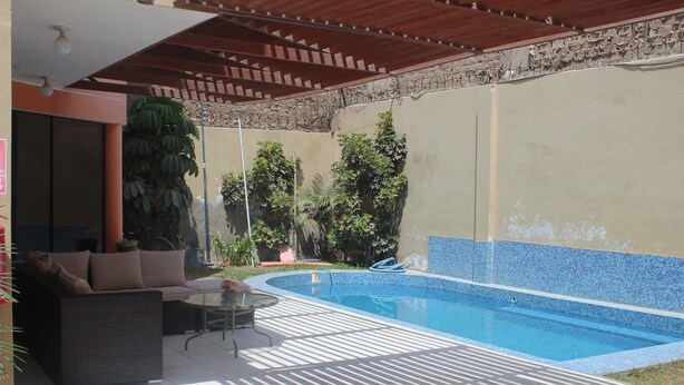 A covered outdoor area with a swimming pool, a patio with furniture, and potted plants. - Hostal Shalom (Pisco)