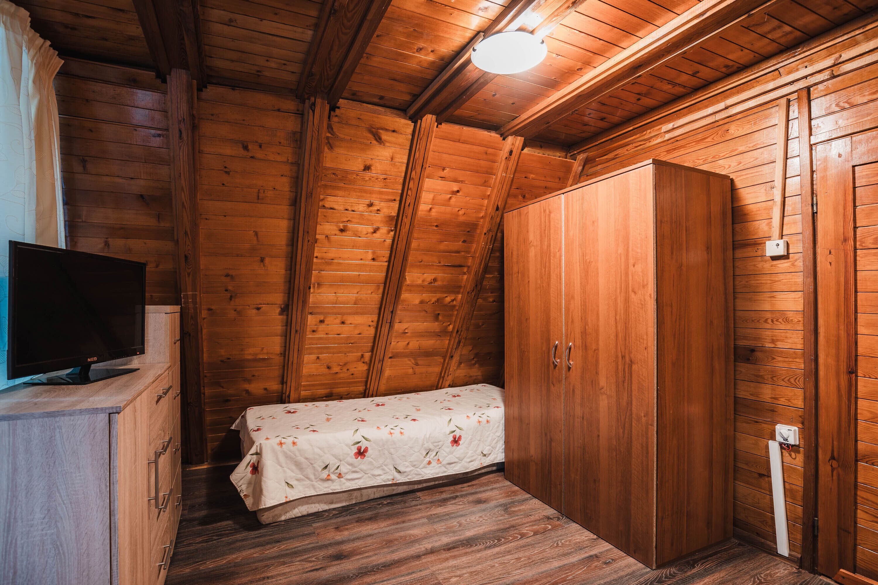 Une chambre dans un chalet en bois, équipée d’un lit, d’une télévision et d’une armoire.