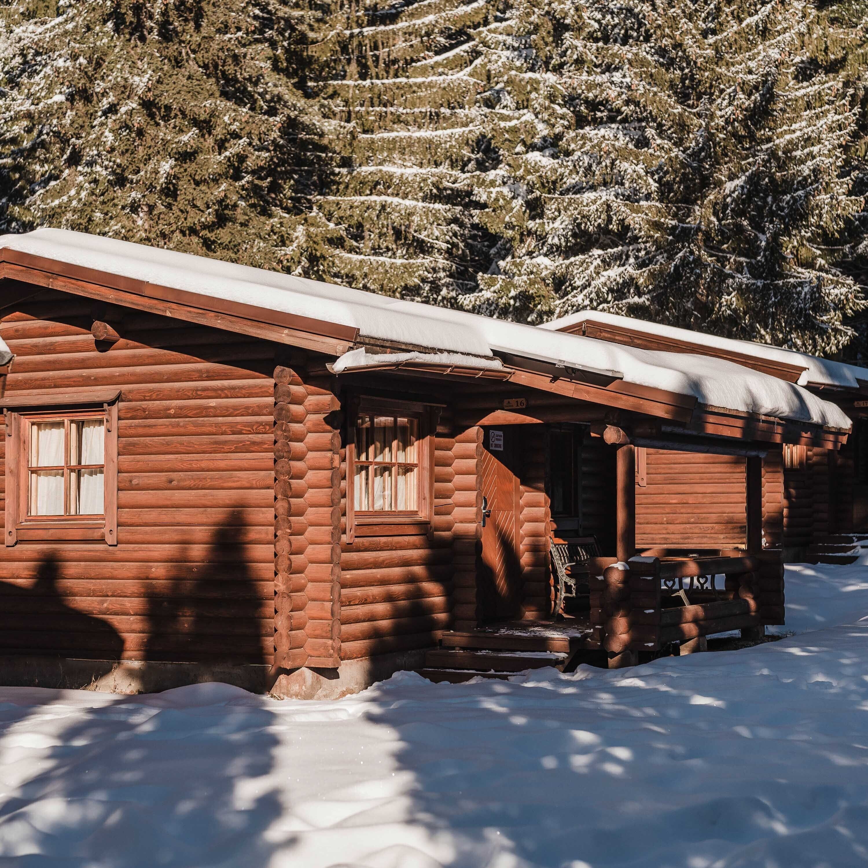 Une cabane en bois, dont le toit est recouvert de neige, entourée d’arbres également couverts de neige.