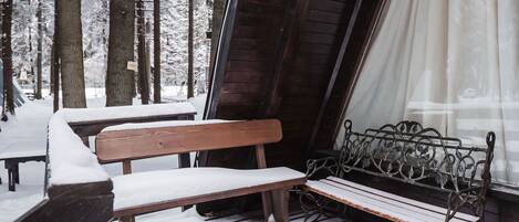 A wooden bench and a metal bench covered in snow, with a window and a curtain in the background.