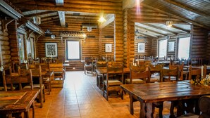 Un intérieur rustique en bois, avec de nombreuses tables et chaises en bois, de grandes fenêtres et des œuvres d’art encadrées accrochées aux murs.