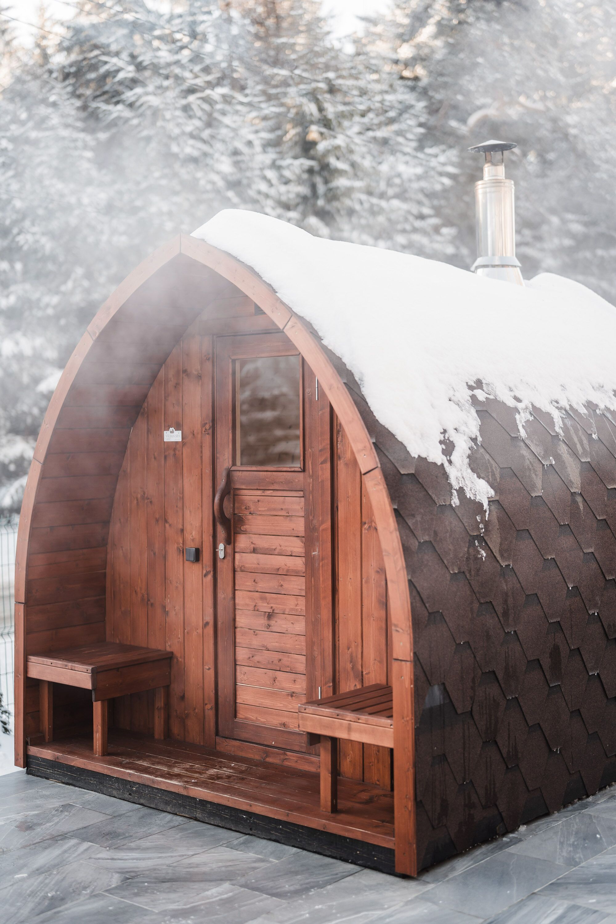 Een houten blokhut met een sneeuwbedekte, schuine dak en een schoorsteen, plus een houten deur.